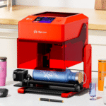 Graveur laser AlgoLaser Pixi rouge gravant une gourde bleue avec module rotatif, entouré d’objets personnalisés sur plan de travail.